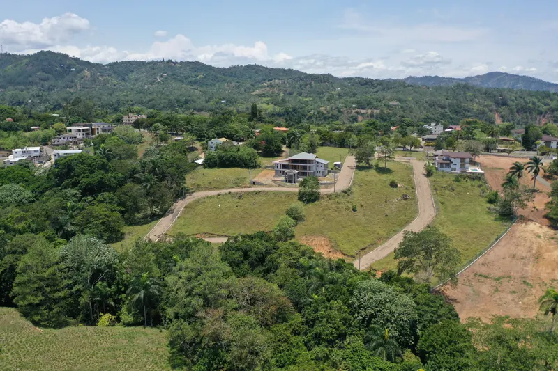 Panorámica de calles imprimadas, contenes, postes y terrenos de la urbanización